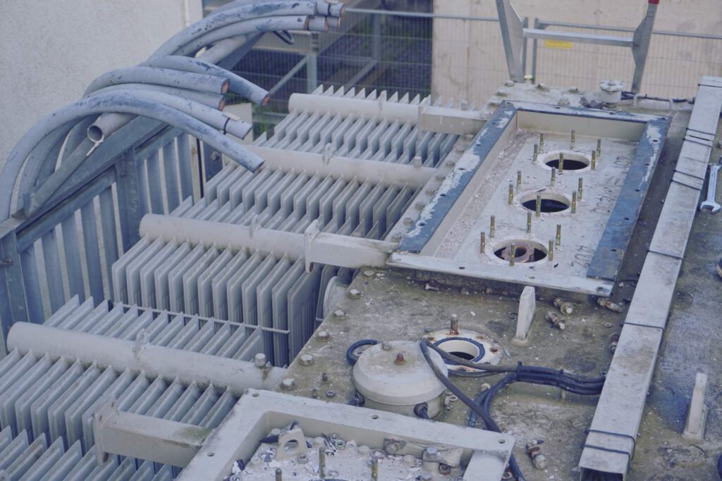 Geöffnete Oberseite eines Transformators mit ausgebauten Bauteilen und abgetrennten Kabeln bei der Demontage.