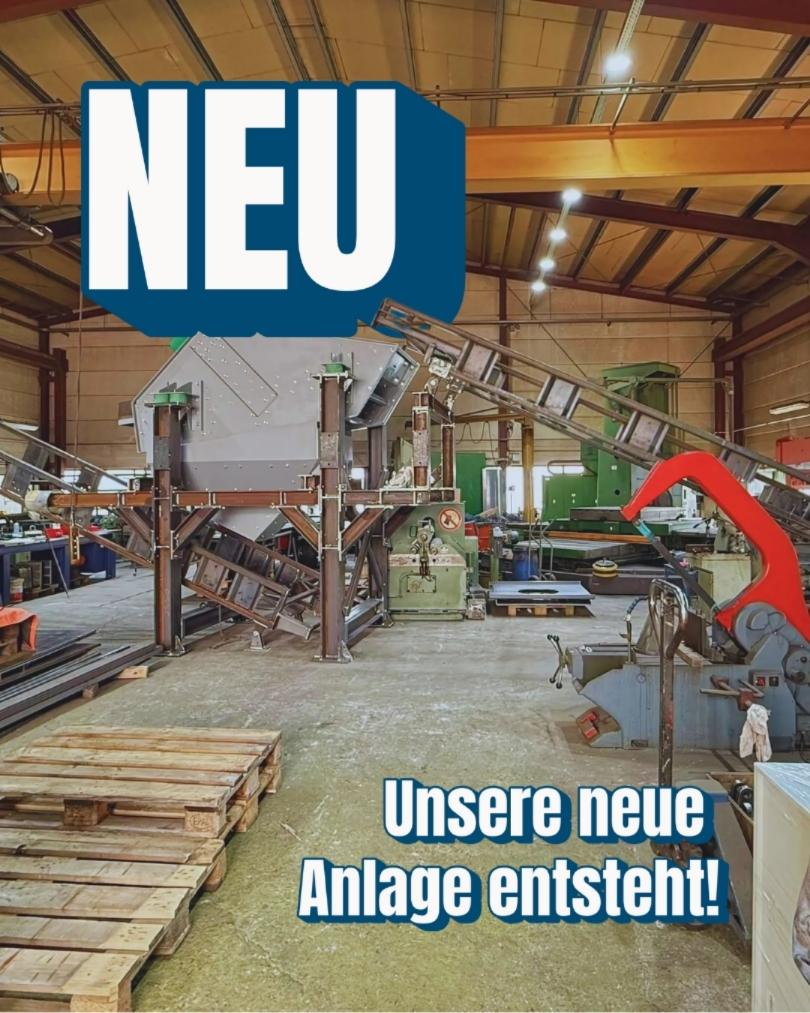 Innenaufnahme einer Werkhalle mit Schotteraufbereitungsanlage im Aufbau; grosser Text „NEU“ und Hinweis „Unsere neue Anlage entsteht!“ sichtbar.