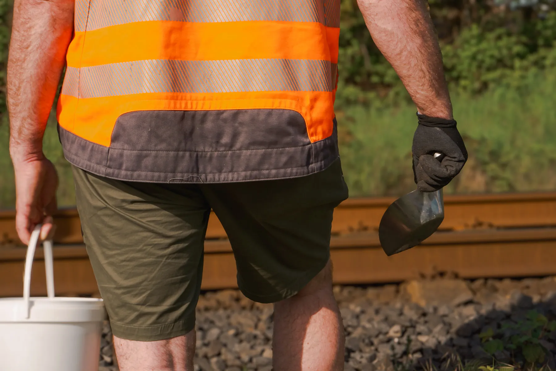 Mitarbeiter trägt Eimer und Probenschaufel am Gleisbett
