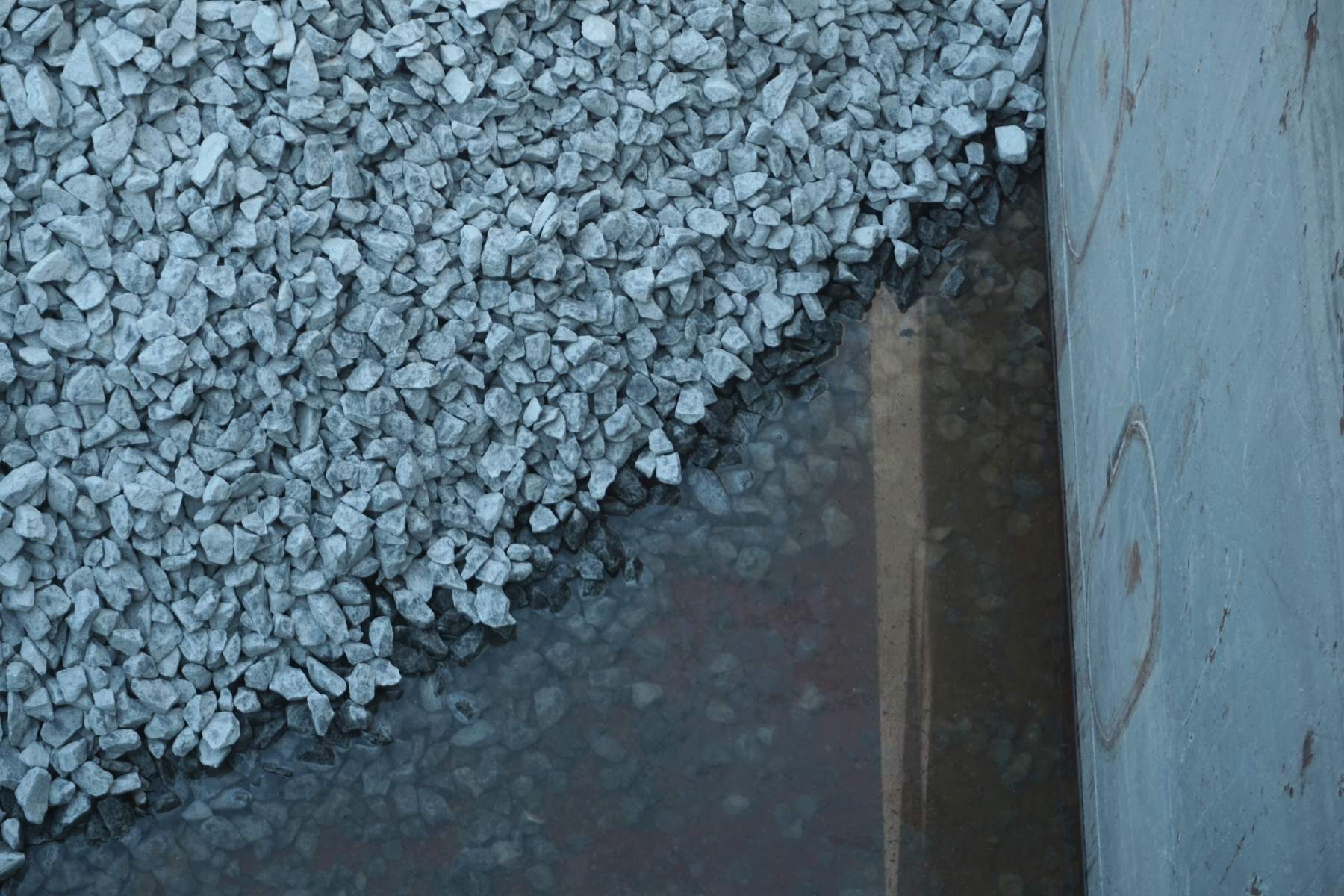 Detail: Schotter in einem metallenen Laderaum, Wasser am Rand