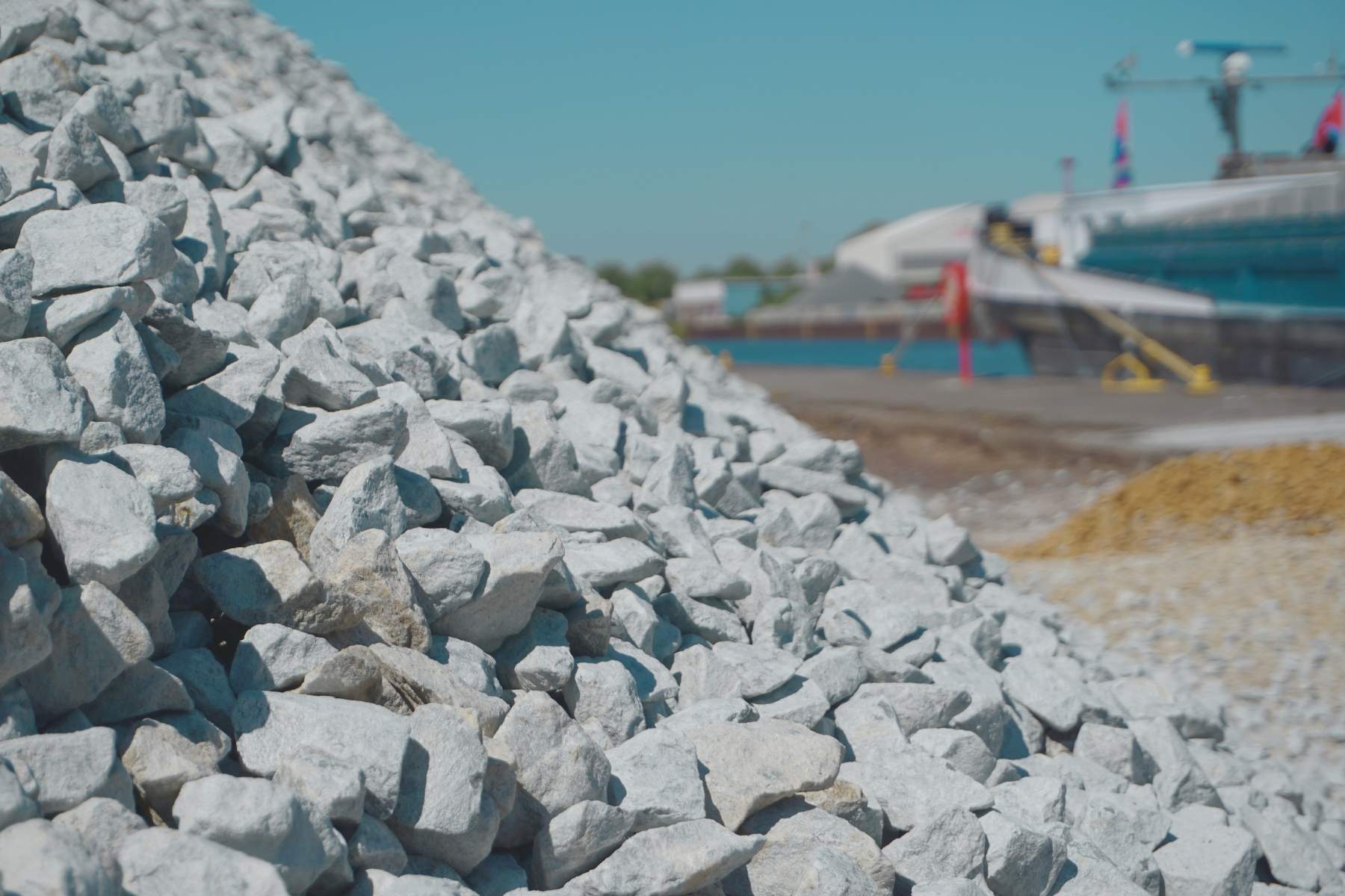 Großer Schotterhaufen im Hafen; Wasser und Umschlagfläche im Hintergrund