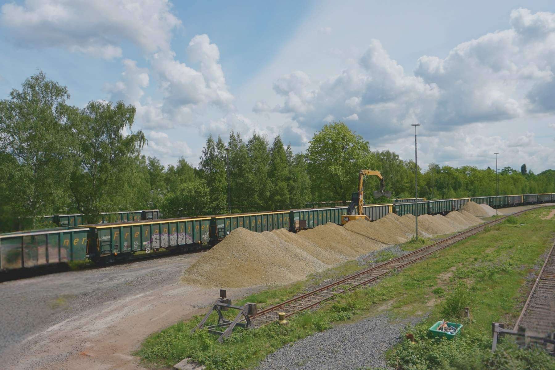 Reihe von Schotterhaufen entlang eines Wagenzugs am Umschlagplatz