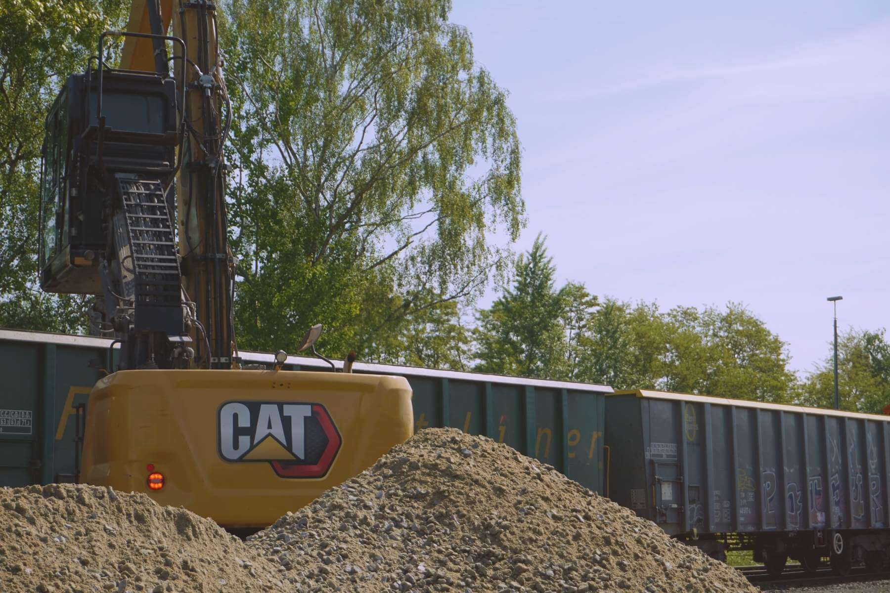 Bagger am Gleis lädt Schüttgut neben Güterwagen um