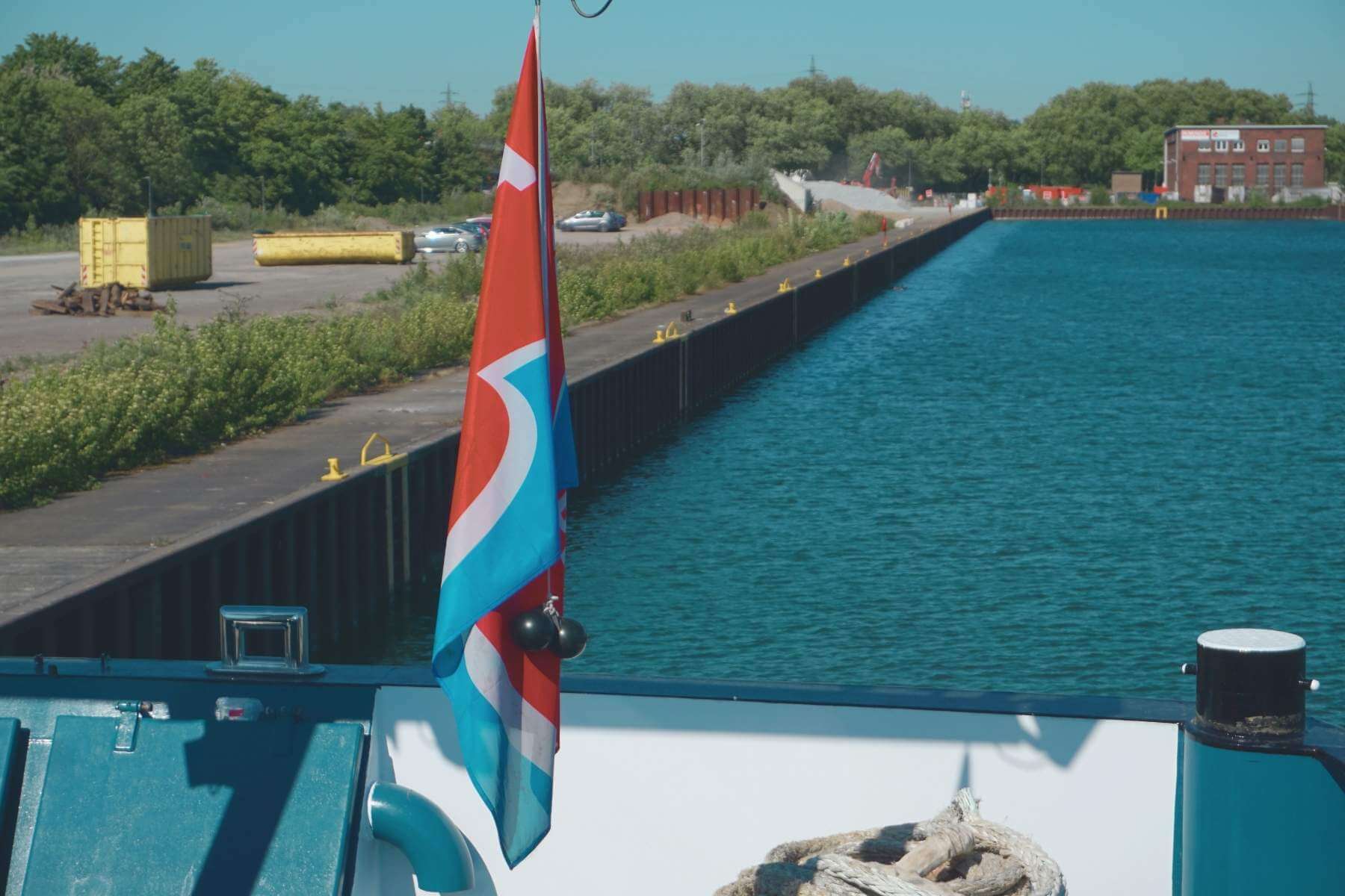 Blick vom Frachtschiff auf ein Hafenbecken mit Kaianlage; Flagge im Vordergrund