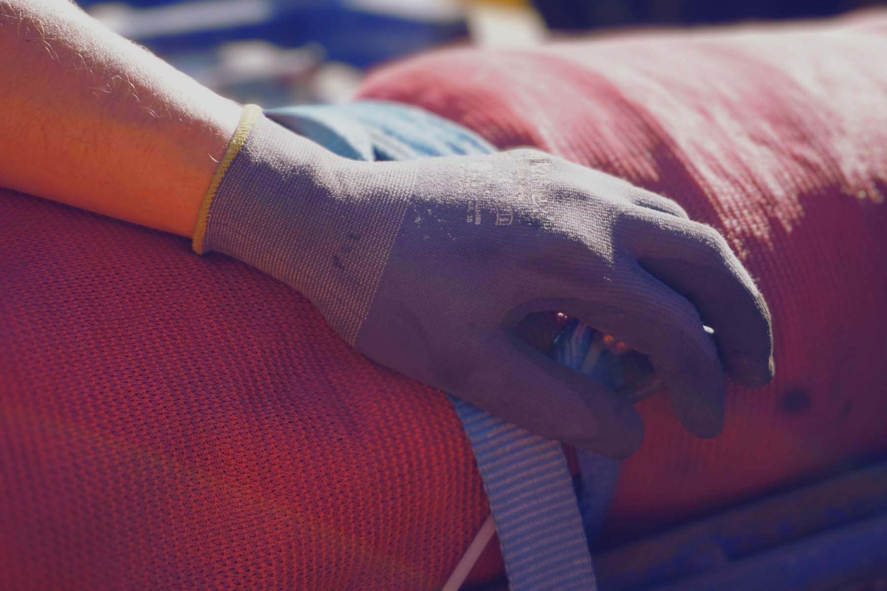 Arbeitshandschuh spannt einen Zurrgurt auf roter Schutzmatte – Detail der Ladungssicherung.