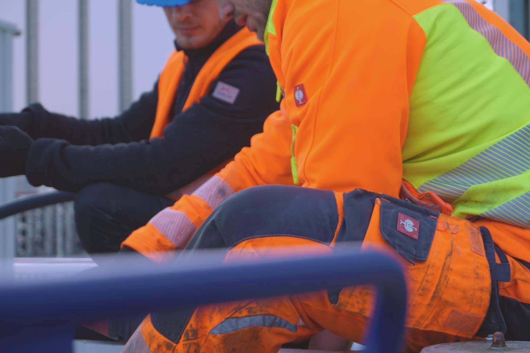 Mitarbeitende in Warnkleidung sitzen zusammen und besprechen Arbeitsschritte.