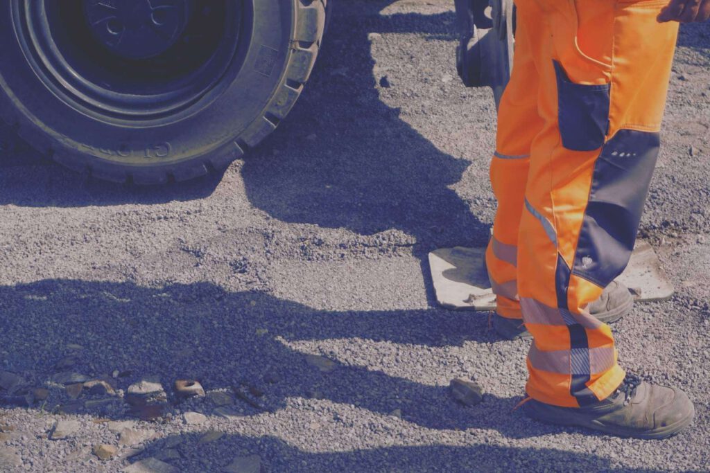 Bauarbeiter in Warnkleidung neben Reifen eines Schwerlastfahrzeugs in NRW